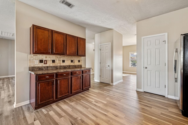 kitchen with visible vents, decorative backsplash, dark countertops, freestanding refrigerator, and light wood-type flooring