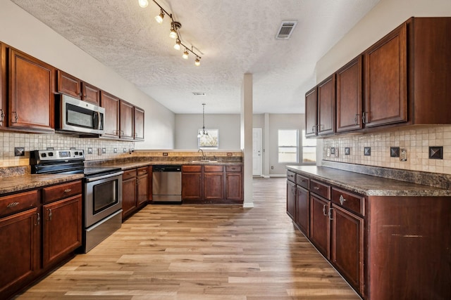 kitchen featuring visible vents, dark countertops, stainless steel appliances, light wood-type flooring, and a sink