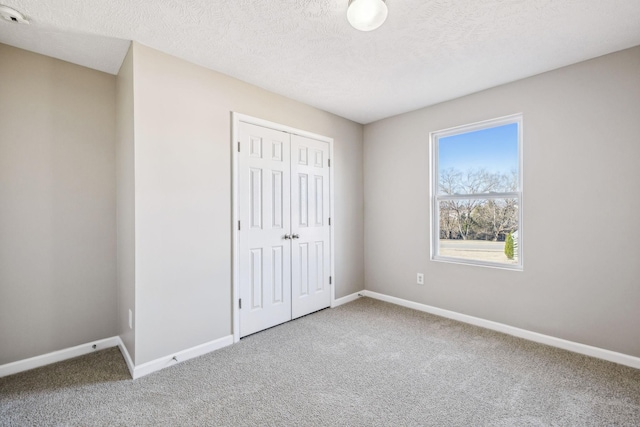 unfurnished bedroom featuring carpet floors, a textured ceiling, baseboards, and a closet