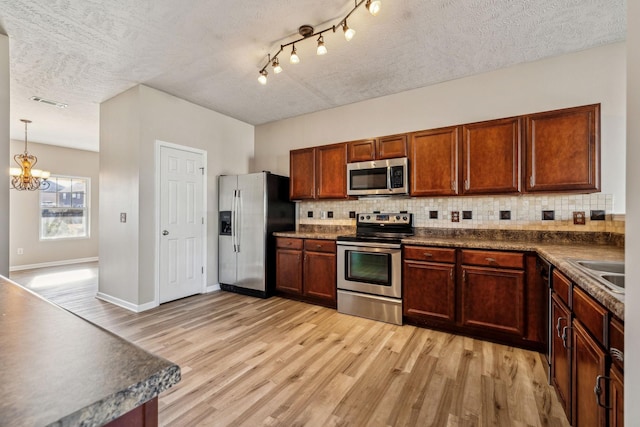 kitchen featuring a textured ceiling, stainless steel appliances, light wood-type flooring, tasteful backsplash, and dark countertops