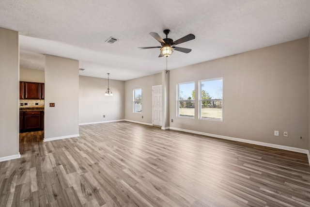 unfurnished living room featuring visible vents, a ceiling fan, a textured ceiling, wood finished floors, and baseboards