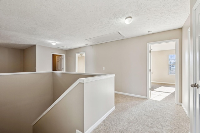 hall featuring attic access, carpet flooring, a textured ceiling, an upstairs landing, and baseboards