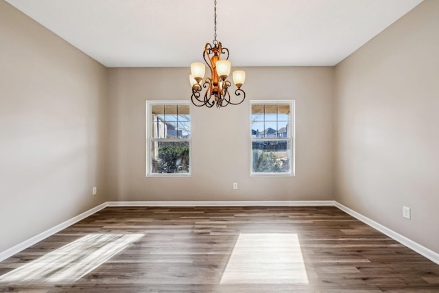 spare room with a chandelier, baseboards, and wood finished floors