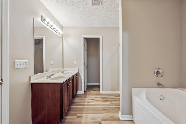 bathroom with a bathtub, double vanity, a sink, a textured ceiling, and wood finished floors