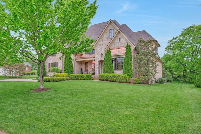 view of front of property with a front yard, a standing seam roof, and brick siding