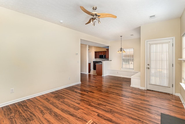 unfurnished living room featuring visible vents, baseboards, dark wood-style flooring, and ceiling fan with notable chandelier