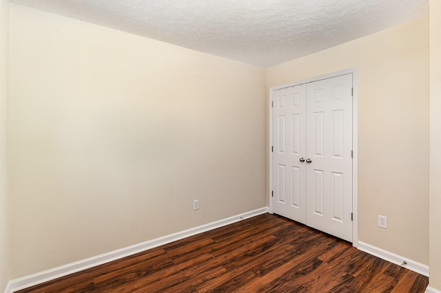 unfurnished bedroom with a closet, dark wood-style flooring, a textured ceiling, and baseboards