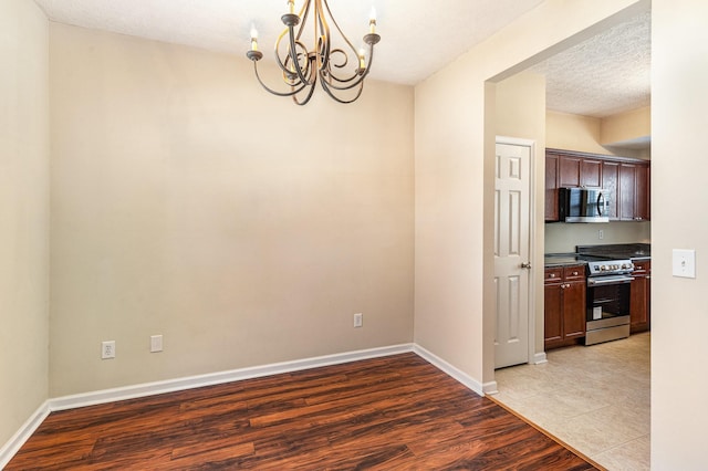 unfurnished dining area featuring baseboards, a textured ceiling, light wood-style flooring, and a notable chandelier