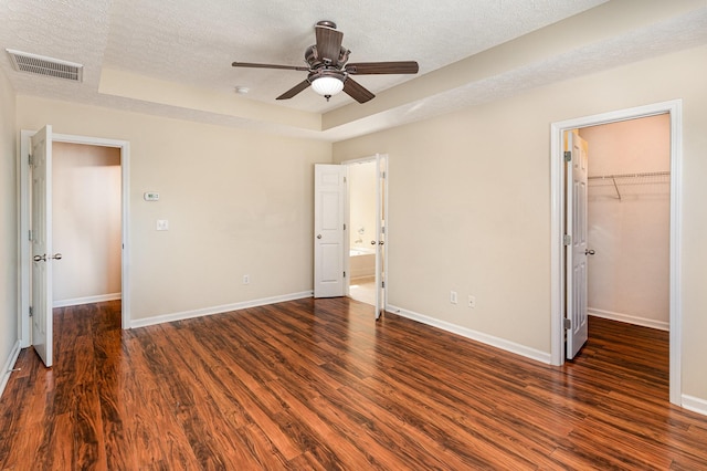 unfurnished bedroom featuring a textured ceiling, a tray ceiling, wood finished floors, and visible vents