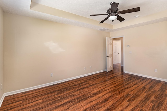 empty room featuring a textured ceiling, a ceiling fan, baseboards, a tray ceiling, and dark wood finished floors