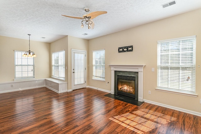 unfurnished living room featuring visible vents, a fireplace with flush hearth, wood finished floors, a textured ceiling, and ceiling fan with notable chandelier