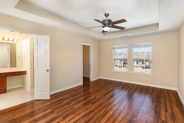 unfurnished bedroom featuring baseboards, a textured ceiling, a tray ceiling, and wood finished floors