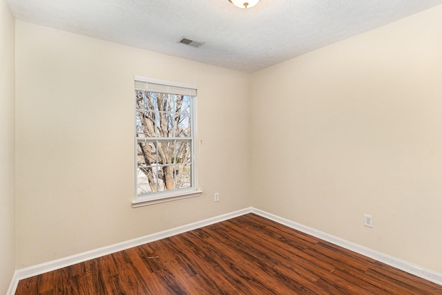 empty room featuring dark wood-style flooring, visible vents, a textured ceiling, and baseboards