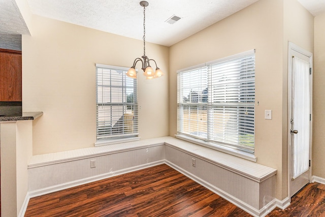 unfurnished dining area featuring a textured ceiling, a chandelier, visible vents, baseboards, and dark wood-style floors