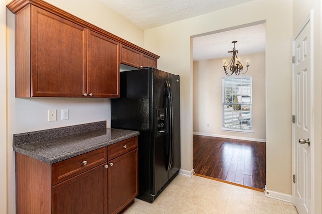 kitchen with hanging light fixtures, a textured ceiling, a chandelier, baseboards, and black fridge