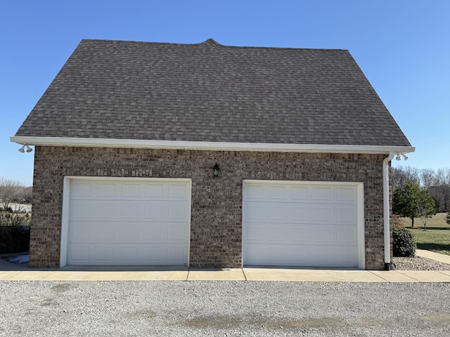 view of side of home featuring a shingled roof, brick siding, and a detached garage