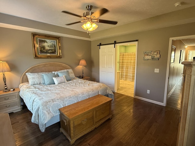 bedroom featuring a barn door, baseboards, a ceiling fan, dark wood-type flooring, and ensuite bathroom