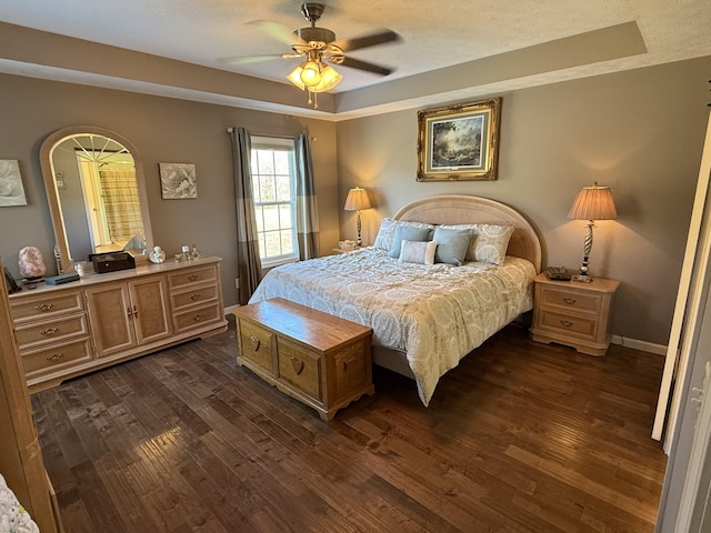 bedroom featuring ceiling fan, a textured ceiling, dark wood-style flooring, baseboards, and a tray ceiling