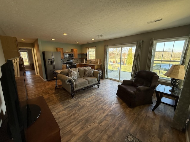 living room featuring dark wood-style floors, visible vents, a textured ceiling, and recessed lighting