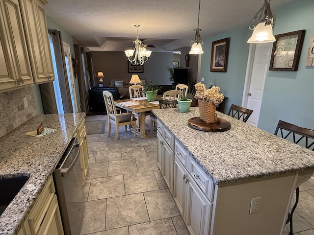 kitchen with stainless steel dishwasher, decorative backsplash, cream cabinetry, and a kitchen breakfast bar