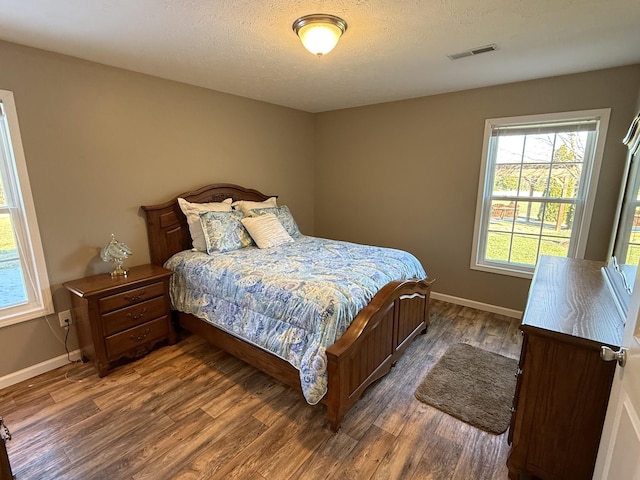 bedroom featuring a textured ceiling, wood finished floors, visible vents, and baseboards