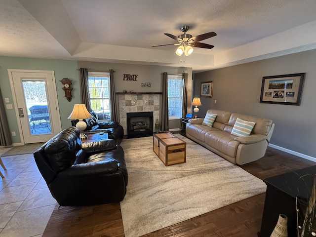 living room featuring baseboards, a tray ceiling, a textured ceiling, and a tile fireplace