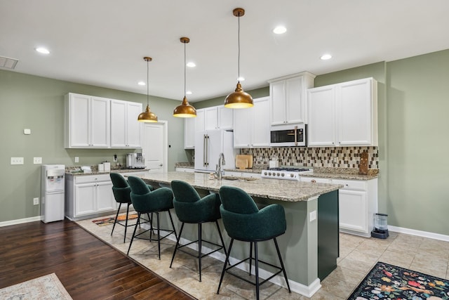 kitchen featuring white appliances, a sink, a kitchen breakfast bar, backsplash, and a center island with sink