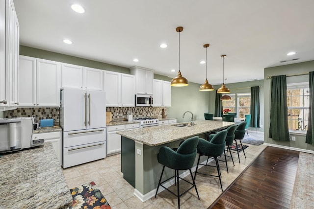 kitchen featuring a kitchen island with sink, white appliances, a sink, white cabinets, and backsplash