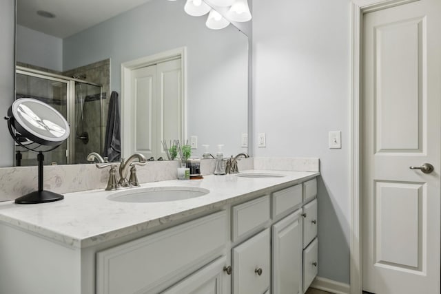 full bath with double vanity, a stall shower, baseboards, and a sink