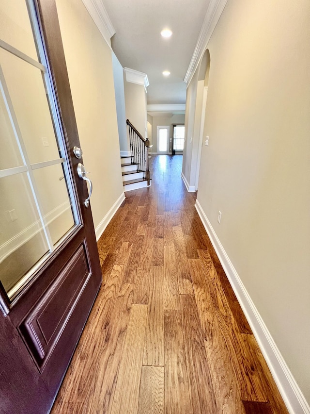 hallway featuring baseboards, arched walkways, ornamental molding, wood finished floors, and stairs