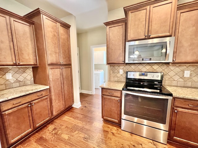 kitchen featuring stainless steel appliances, tasteful backsplash, light wood-style flooring, and light stone counters