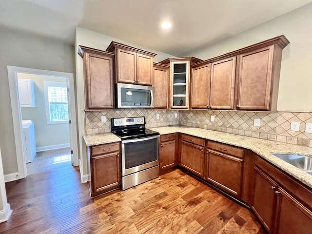 kitchen featuring appliances with stainless steel finishes, light stone counters, decorative backsplash, and wood finished floors