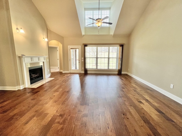 unfurnished living room featuring a high ceiling, a premium fireplace, dark wood-type flooring, a ceiling fan, and baseboards