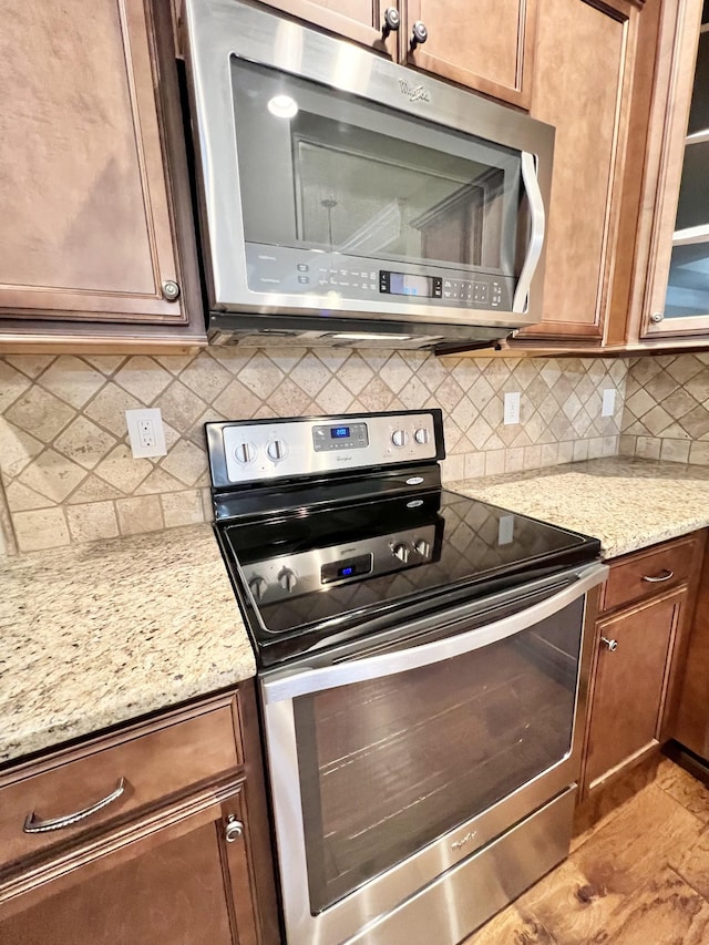 kitchen featuring stainless steel appliances, glass insert cabinets, light stone counters, and tasteful backsplash