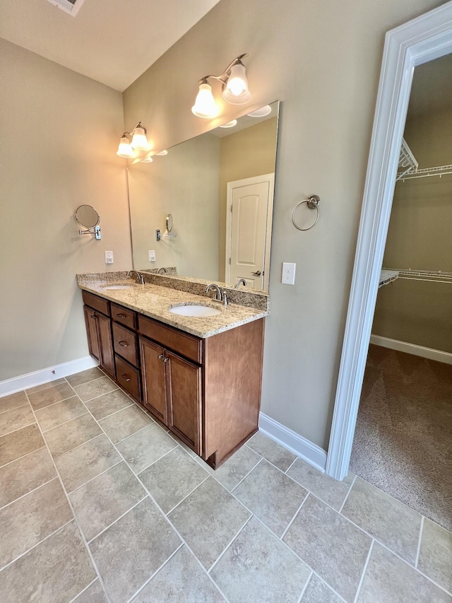 bathroom featuring double vanity, a spacious closet, a sink, and baseboards