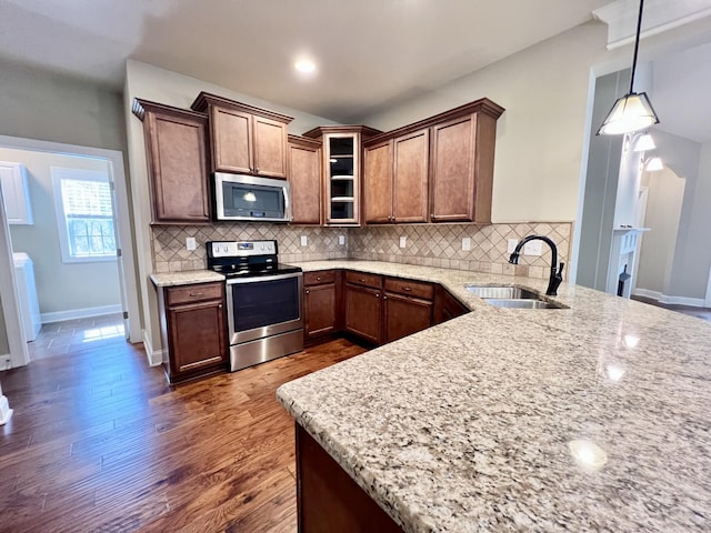 kitchen featuring appliances with stainless steel finishes, a sink, backsplash, and light stone countertops