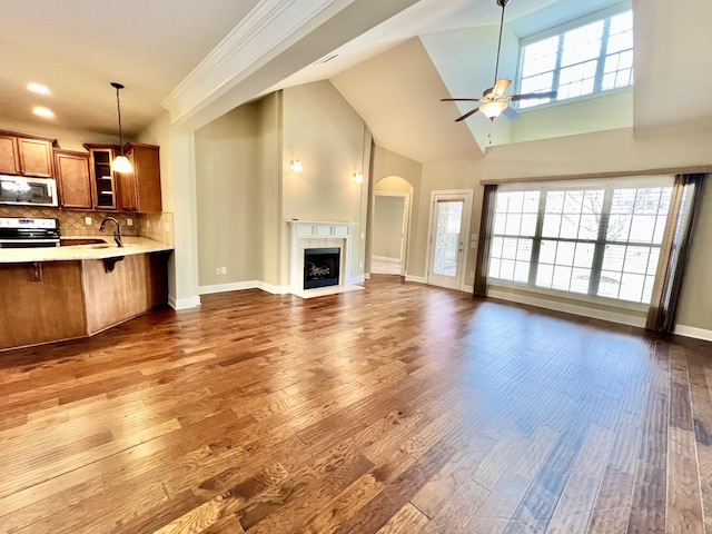 unfurnished living room with baseboards, a ceiling fan, a fireplace with flush hearth, wood finished floors, and a sink