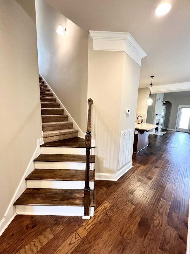 staircase with arched walkways, wood finished floors, visible vents, baseboards, and ornamental molding