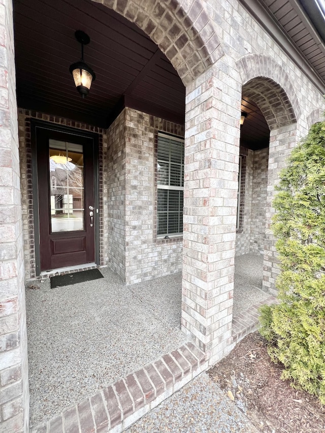 doorway to property featuring brick siding and a porch