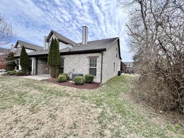 view of home's exterior featuring brick siding, a yard, a chimney, and central AC unit