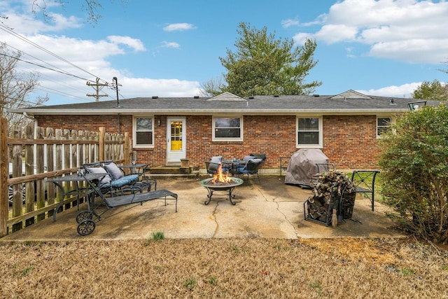 rear view of property with brick siding, fence, a fire pit, and a patio