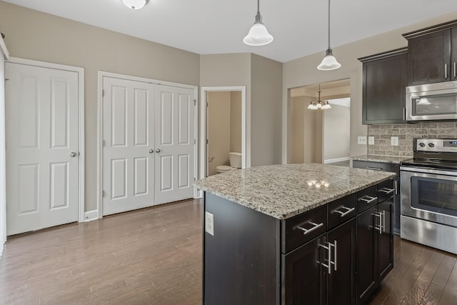 kitchen featuring decorative backsplash, appliances with stainless steel finishes, dark wood-style flooring, hanging light fixtures, and light stone countertops