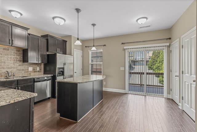 kitchen with dark wood-style floors, stainless steel appliances, backsplash, a kitchen island, and a sink