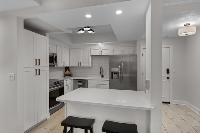 kitchen featuring a breakfast bar area, stainless steel appliances, a sink, decorative backsplash, and a raised ceiling