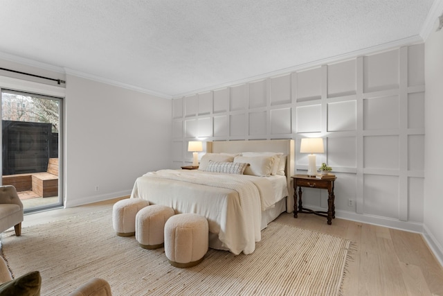 bedroom featuring access to outside, ornamental molding, wood finished floors, and a decorative wall