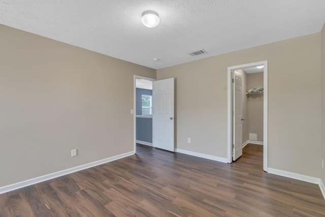 unfurnished bedroom with dark wood-style flooring, visible vents, and baseboards