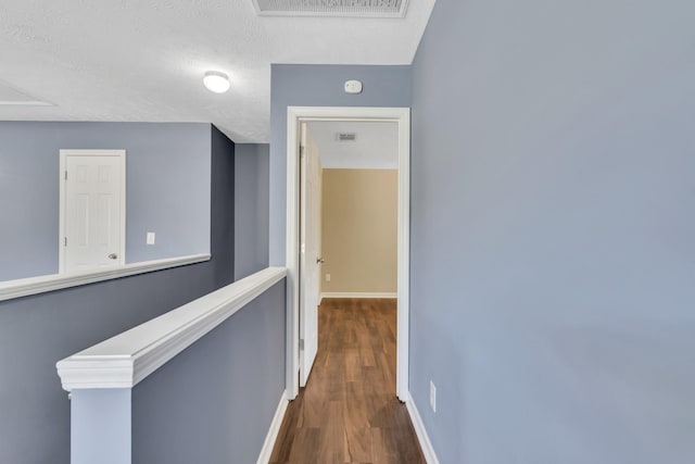 corridor with visible vents, a textured ceiling, baseboards, and dark wood-style flooring