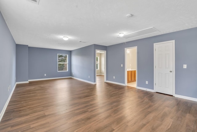 empty room featuring dark wood-style floors, attic access, baseboards, and a textured ceiling