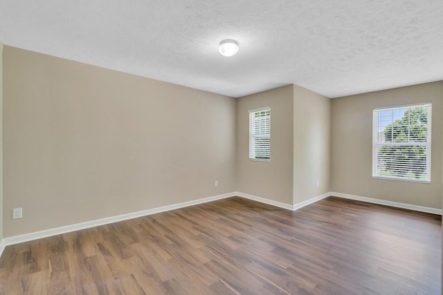 empty room with a textured ceiling, dark wood-style flooring, and baseboards