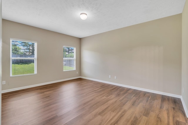 empty room featuring a textured ceiling, baseboards, and wood finished floors